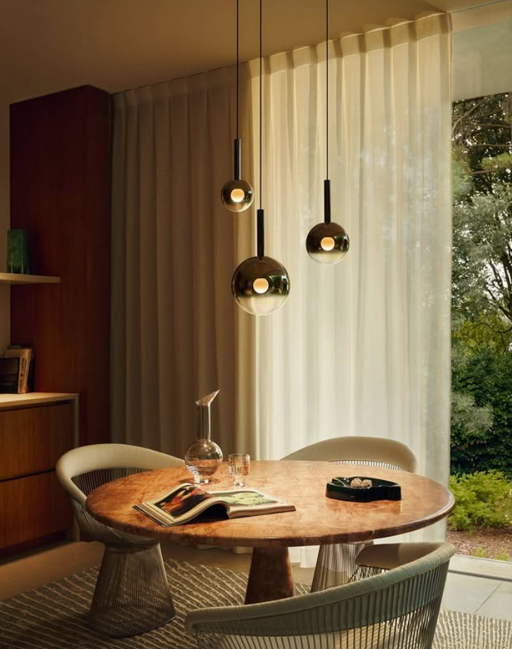 A modern chandelier with gradient glass globes in a spiral arrangement, hanging in a high ceiling room with a cityscape view.