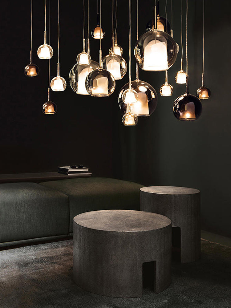 A modern chandelier with spherical glass shades and metallic structure, hanging at varying heights over a dining table, with warm light diffused throughout the space.