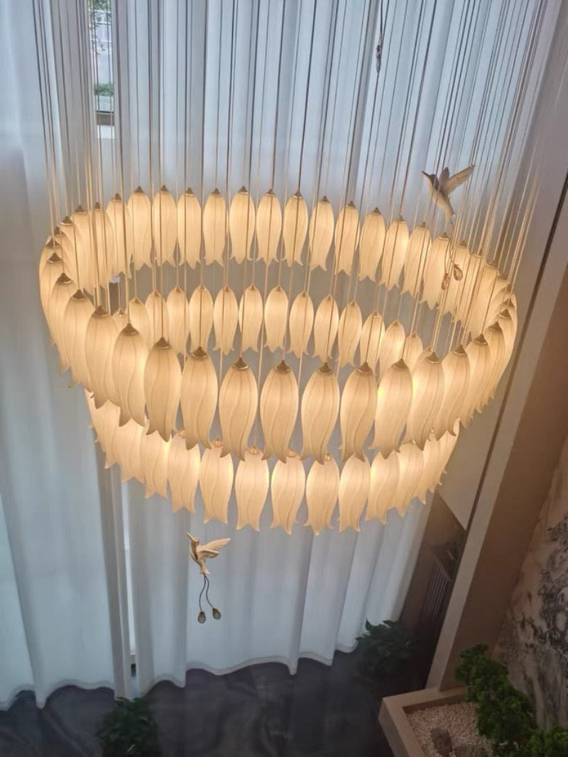 Luxurious ceramic flower chandelier illuminating stairway with layered petals and hummingbird accents for foyer entryway,warm light illuminates the scene (real photos).