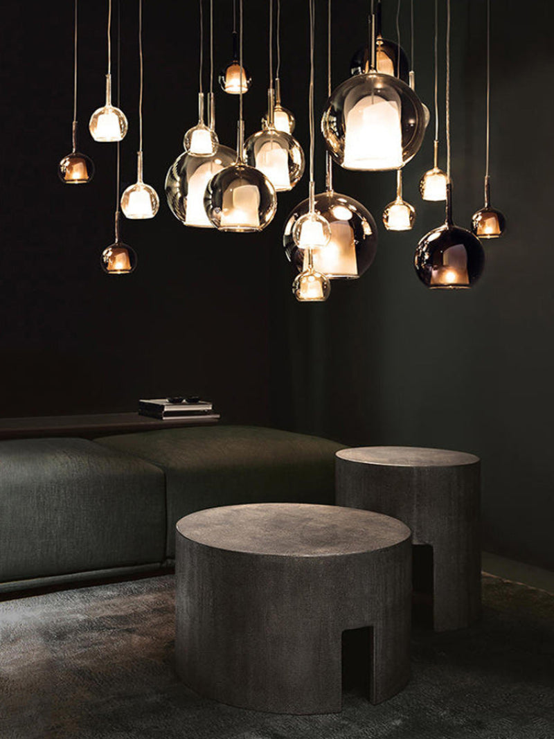 A modern chandelier with spherical glass shades and metallic structure, hanging at varying heights over a dining table, with warm light diffused throughout the space.