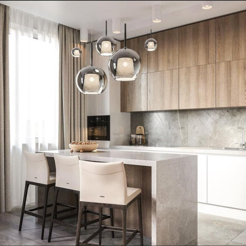 A modern chandelier with spherical glass shades and metallic structure, hanging at varying heights over a dining table, with warm light diffused throughout the space.