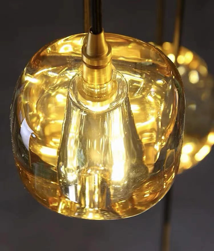 An amber-colored, square crystal chandelier with a spiral design, suitable for high-ceilinged spaces such as stairwells, foyers, and entryways.
