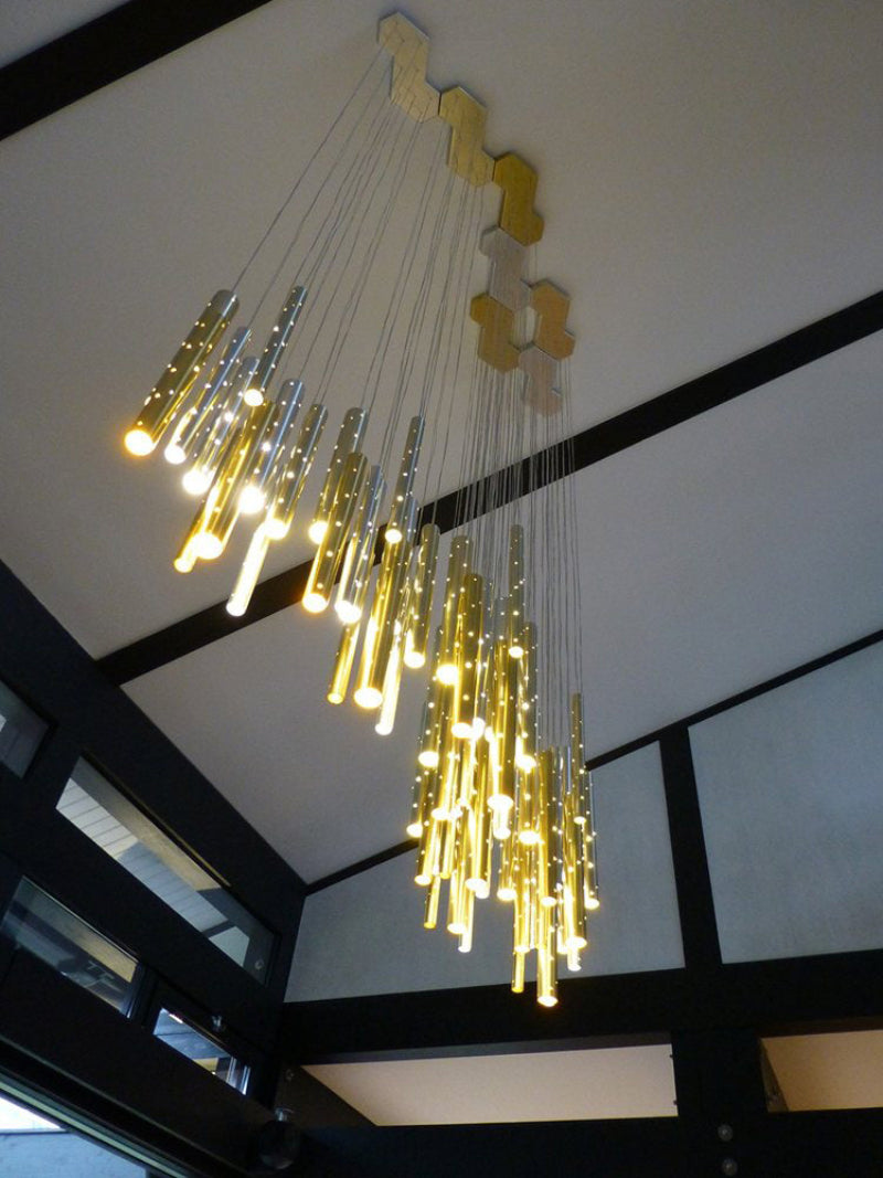 Gold linear cylinder chandelier in foyer, modern meteor shower design with perforated tubes for entryway staircase