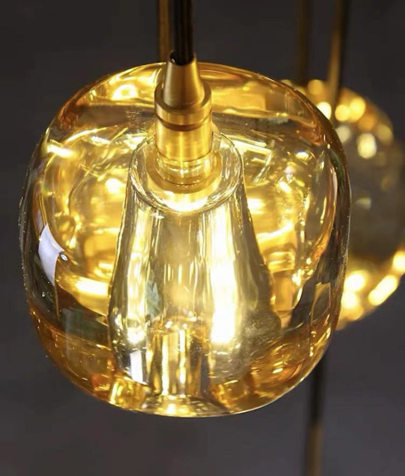 An amber-colored, square crystal chandelier with a spiral design, suitable for high-ceilinged spaces such as stairwells, foyers, and entryways.