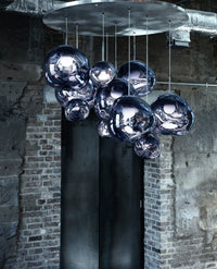 Thumbnail for Modern chandelier with glass balls hanging from a metallic ceiling fixture against a brick wall.