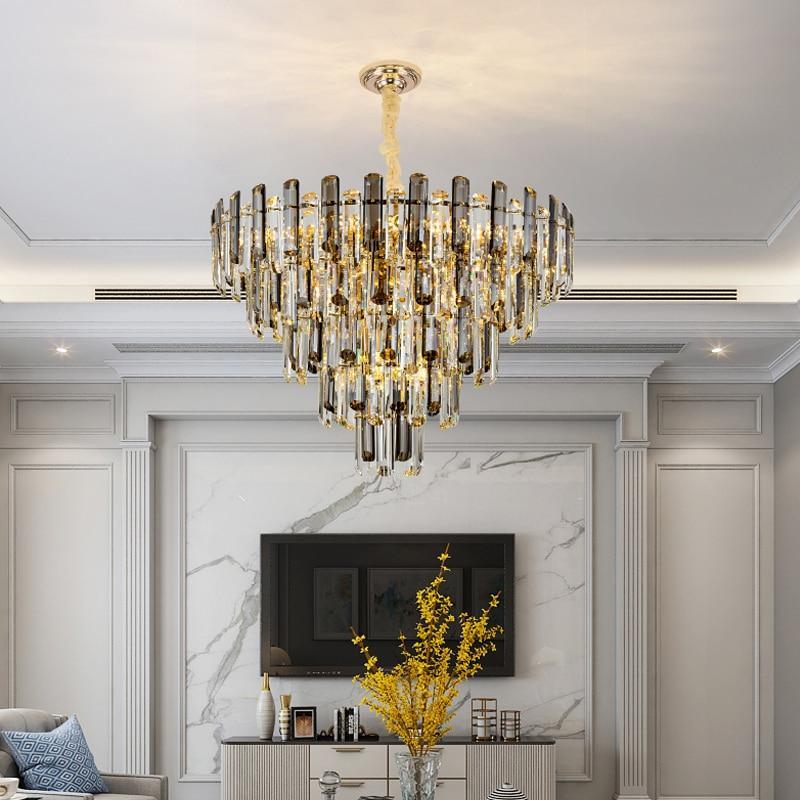 A luxurious modern chandelier with clear and smoky grey crystals, hanging in a spacious room with a high ceiling, marble walls, and a flat ceiling type.