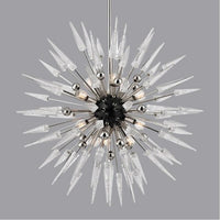Thumbnail for A unique sputnik chandelier with a gold or light grey finish, featuring a round, star-like shape with multiple arms, hanging over a dining table with chairs around it, set against a dark marble wall.